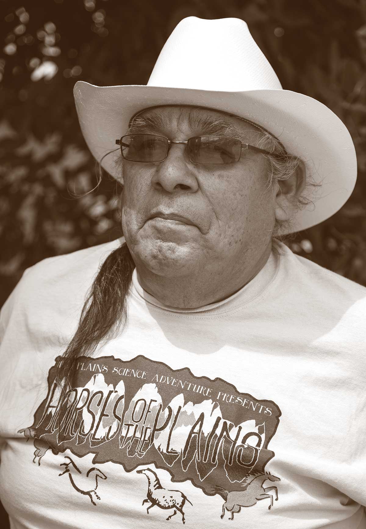 A photograph of a seated man wearing a cowboy-style hat and sunglasses