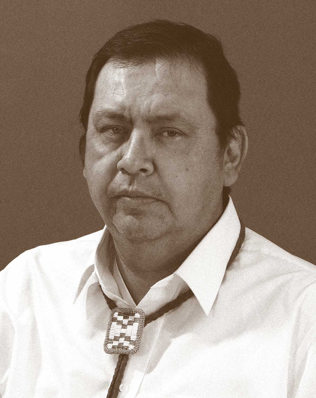 Photograph of a man in a white collared shirt with a bolo necktie