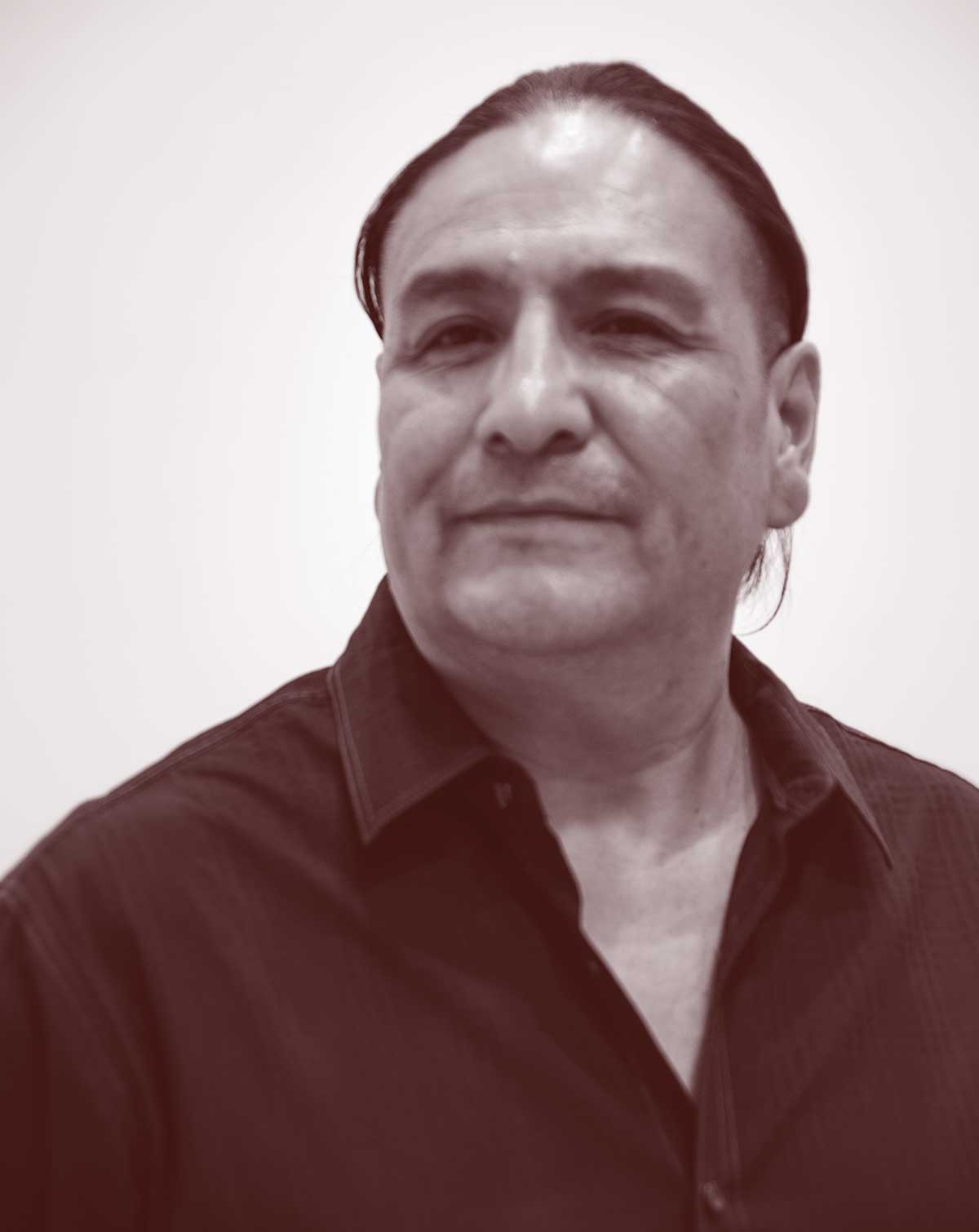 A photo of a man with hair tied back, wearing a dark collared shirt