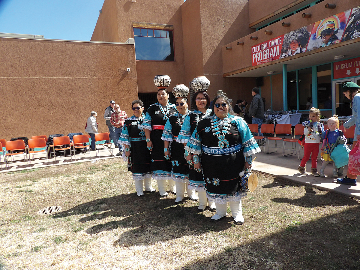 Five Zuni dancers stand in a line, three of them balancing pots on their heads