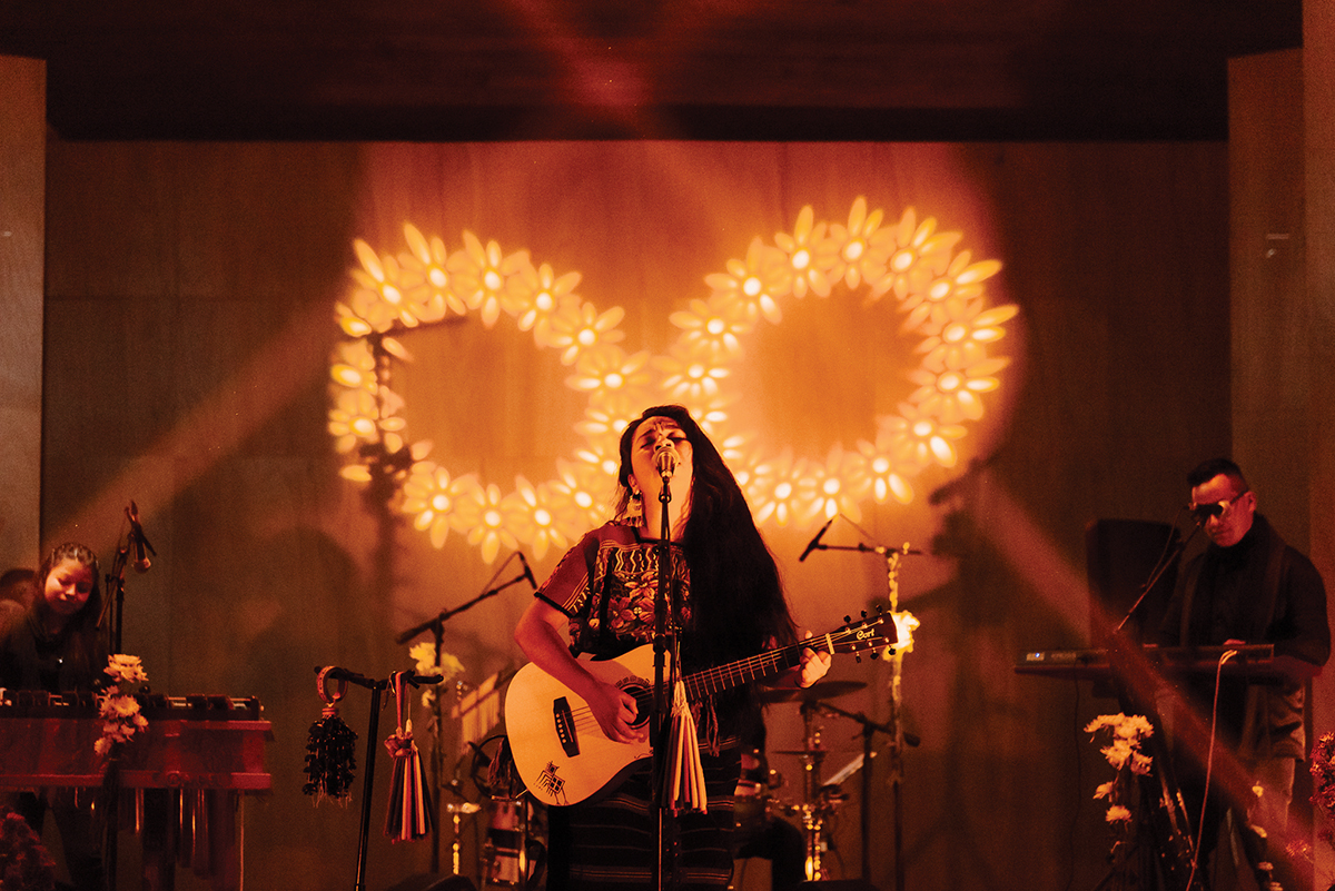 A singer with a guitar performing on a stage lit with golden light