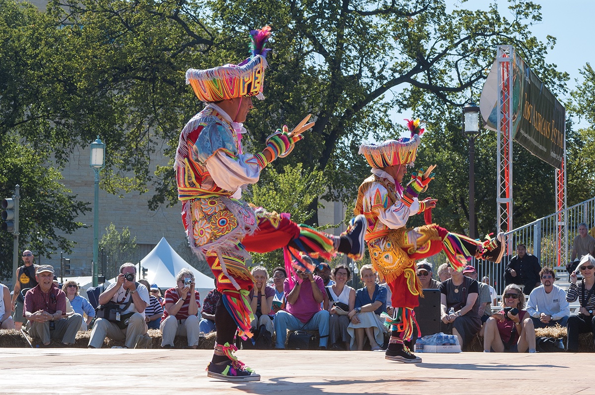 Peruvian dancers in bright costumes perform outdoors in front of an audience