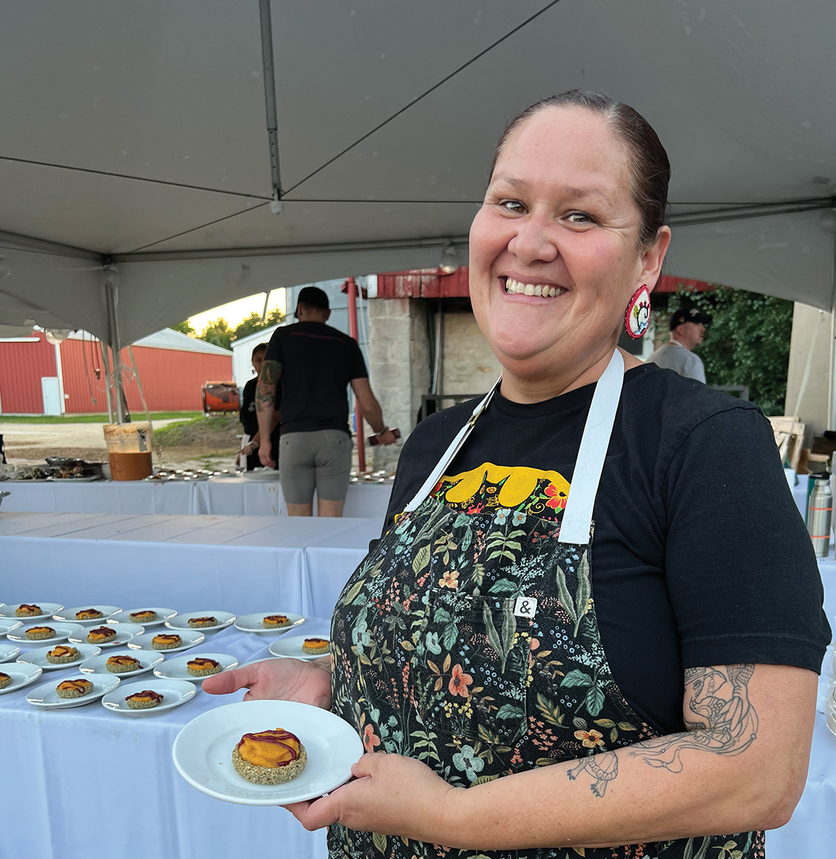 A smiling woman in an apron, holding a plate of food