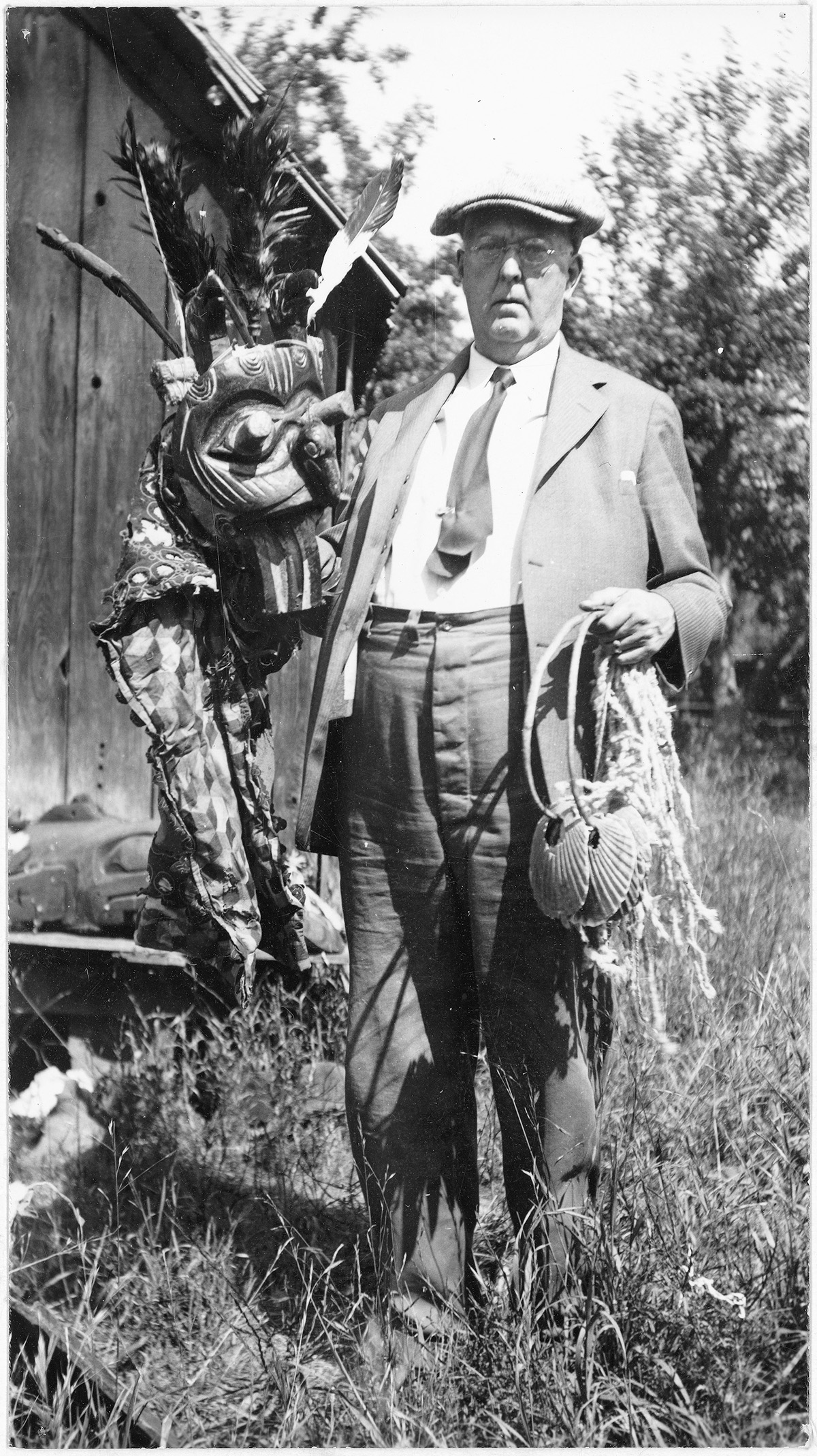 Black and white photo of George Heye holding a mask and rattle