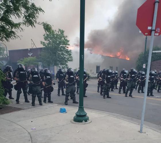 Policemen standing in front of the burning MIGIZI building in Minneapolis.