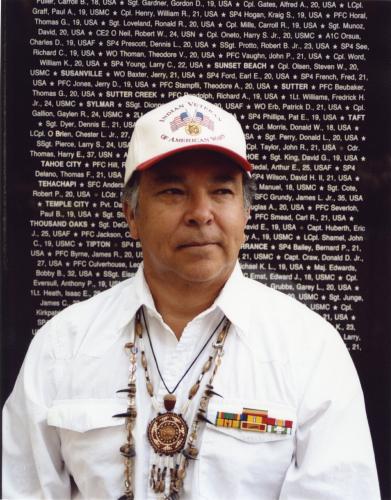 Aguilar is photographed from the chest up, posed in front of a black slab etched with white names.