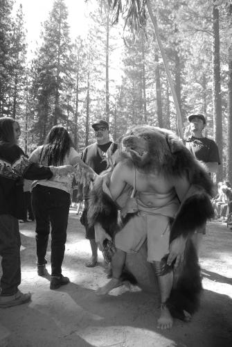 A black and white image of a man wearing the skin and head of a bear.