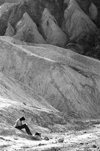 A black and white photograph of a rocky landscape, with a woman sitting at the bottom of a hill.
