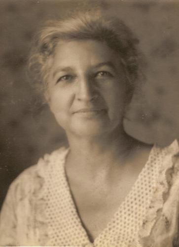 A sepia-toned portrait of Jennie Ross Cobb taken about 1945. She wears a light colored blouse with a v-neck ruffled collar and is smiling softly.