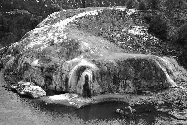 A black and white image of a large rock formation near the water.