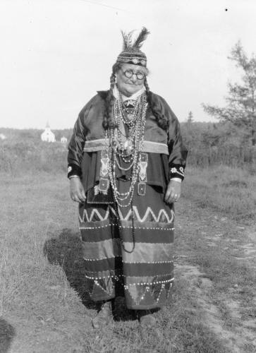A black and white image of a woman in a beaded skirt, jacket and feathered hat
