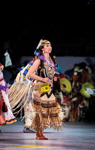 A female dancer wearing a basket hat and buckskin dress