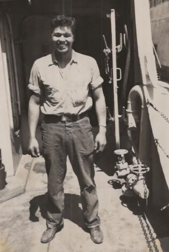 A black and white photograph of a smiling man on the deck of a Navy ship