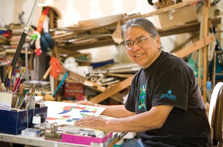 An artist in his studio, seated at a work table