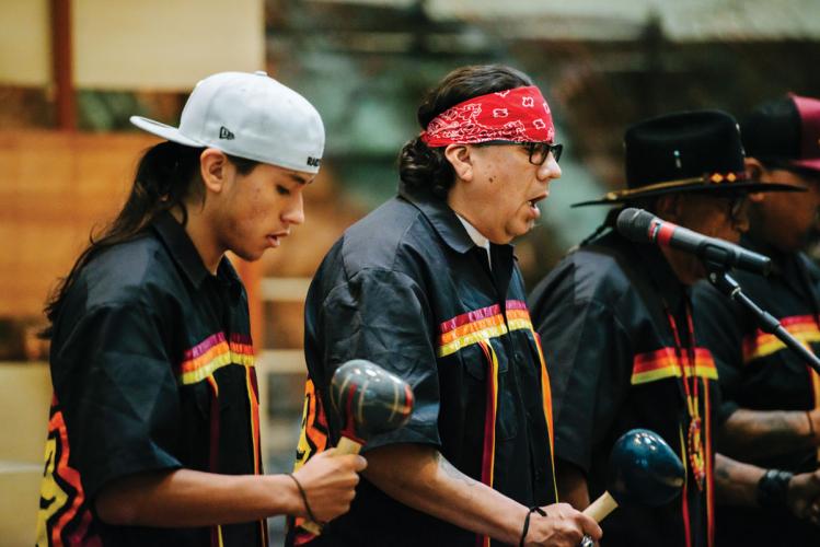 A group of musicians performing, wearing black jackets with a yellow, orange, and red stripe