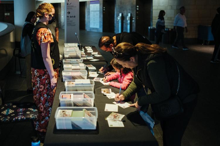 Two adults and a child write postcards at a table