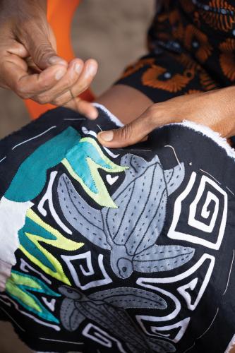 A woman sews leatherback turtle designs onto a textile