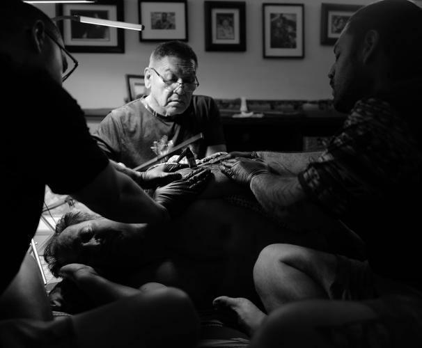 A traditional tattoo artist at work, helped by two assistants