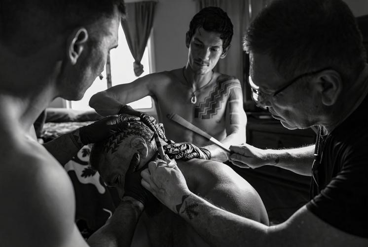 A traditional tattoo artist applies a tattoo with the help of two assistants