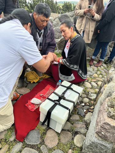 Three people on a stone path crouch over a box holding ancestral remains