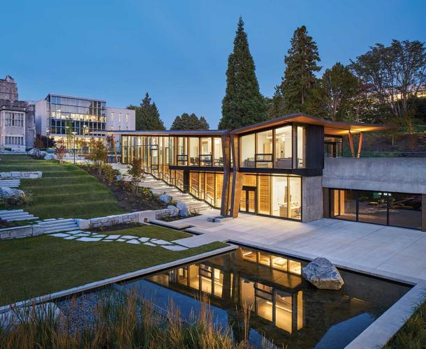 The exterior of a building illuminated at dusk, with a garden pond nearby