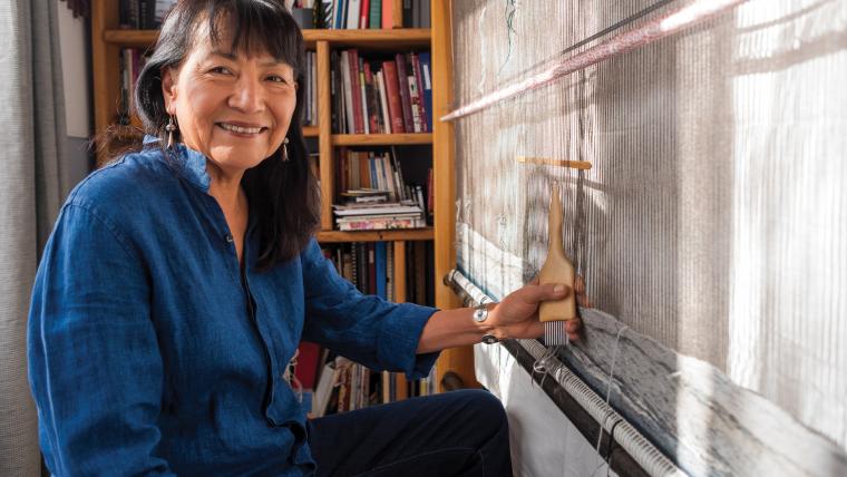 Artist DY Begay smiling while working on a large weaving in her studio.