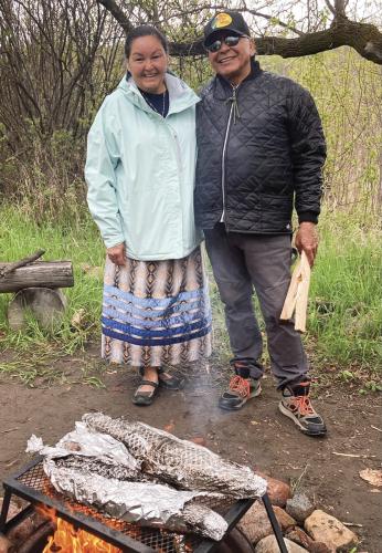 Tim Eashappie and his wife Kathy stand beside fish wrapped in foil cooking over fire.