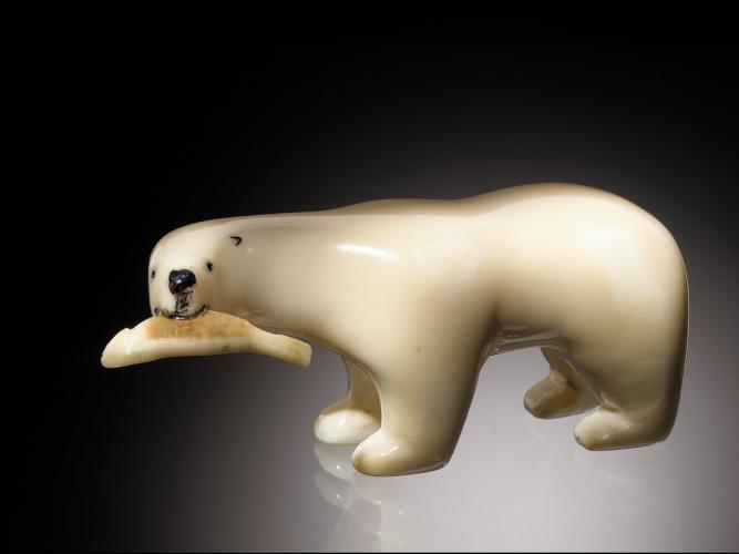An ivory figurine of a polar bear holding a fish in its mouth on a black background.