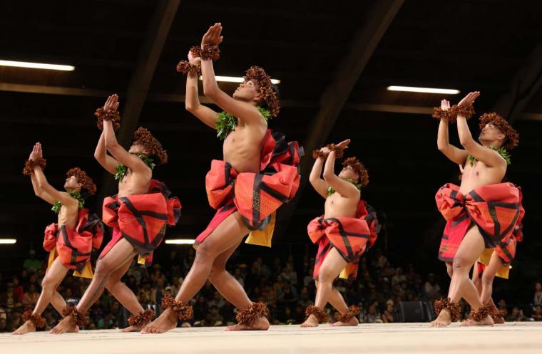 Hula dancers performing on stage in vibrant red and black outfits