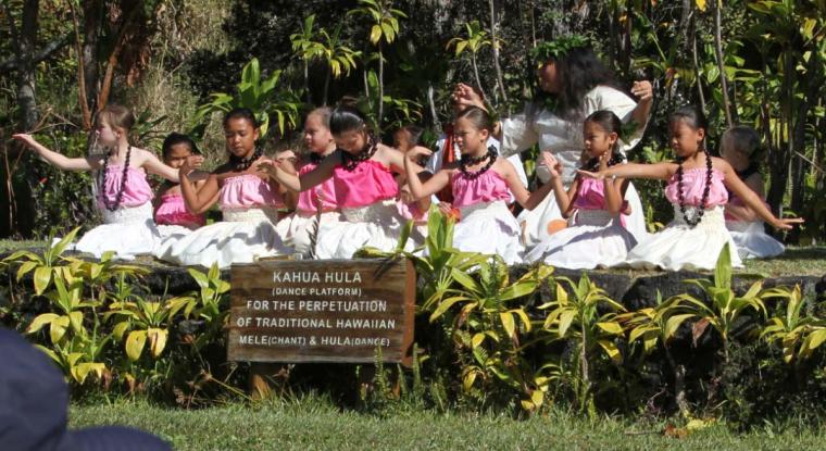 Group of children in white and pink dresses performing hula on stage