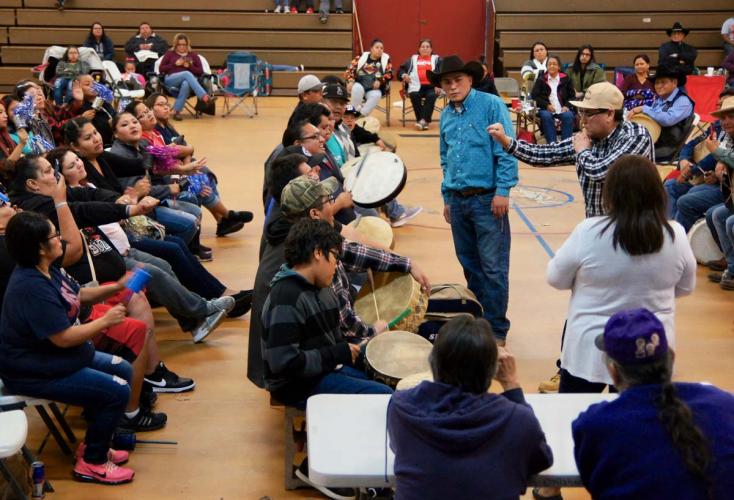 Crowd of people seated in a gymnasium observe participants playing a handgame.