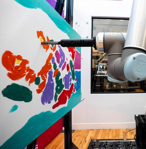 Robot arm equipped with a paint brush paints on a canvas.