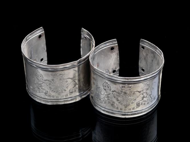 A pair of silver armbands with delicate engravings of an emblem depicting a horse and lion.