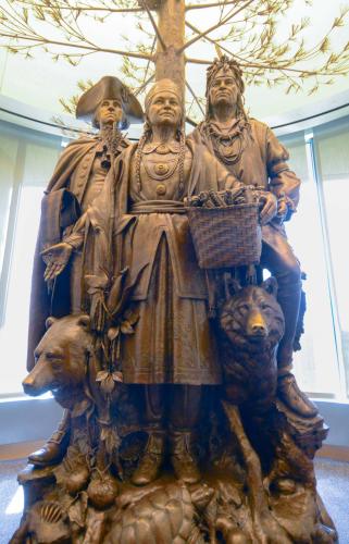 A bronze sculpture depicting Oneida Chief Shenendoah, General George Washington, and Polly Cooper standing under a towering tree amongst fruits and animals.