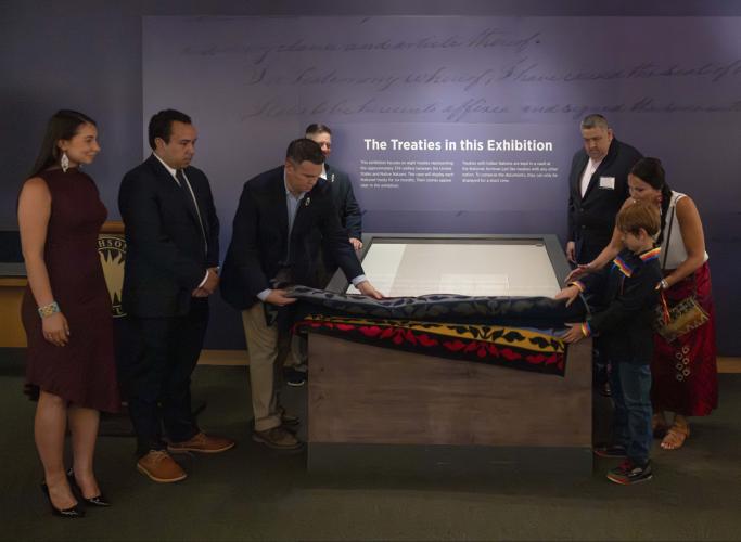 A group of representatives from various Native nations roll up a blanket covering a glass case revealing the Delaware Treaty of 1778.