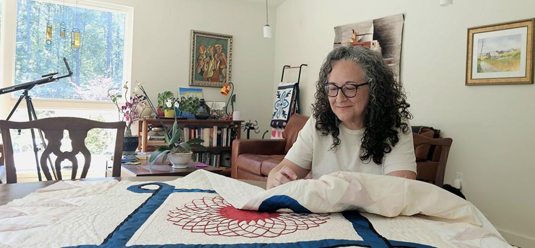 Emma Alcazar sews a red, white, and blue quilt at a table in her sunny, art-filled home.