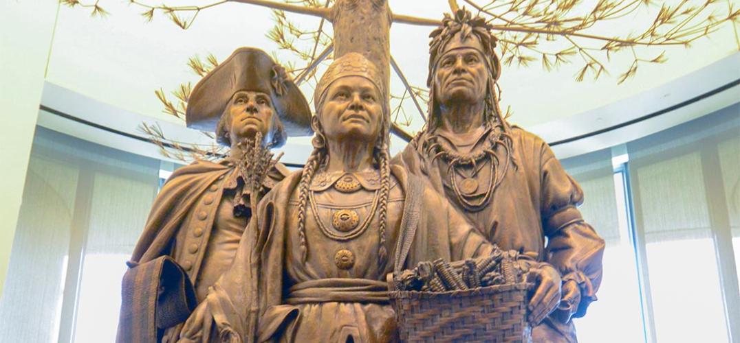 A bronze sculpture depicting Oneida Chief Shenendoah, General George Washington, and Polly Cooper standing under a towering tree amongst fruits and animals.