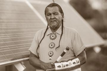 A portrait of Chief Henry Red Cloud standing in front of a solar panel